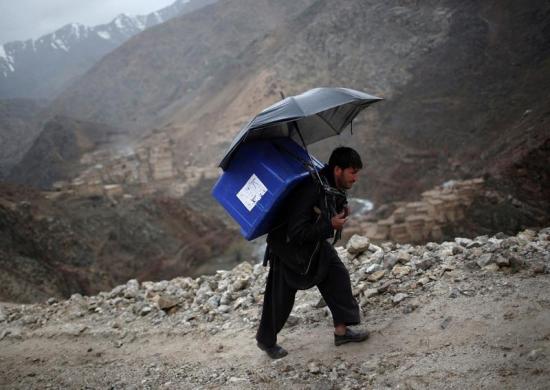 Afghani man backpacking a ballot box up a mountainous trail in the rain