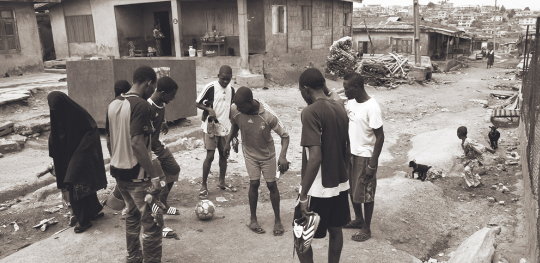 Group of boys playing on a grubby slum street. They and the photographer are oblivious to the woman passing within a few inches of them, a black-shrouded ghost